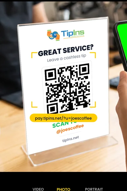 A phone camera scanning a printed TipIns QR sign on a cafe counter